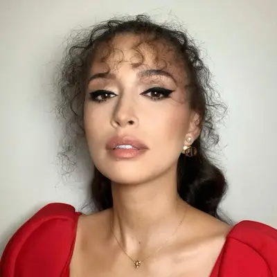 Christian Serratos wears wispy, face-framing curly bangs and a half-up hairstyle