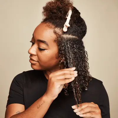 Close up of a MYM Beauty editor sectioning her curly hair and applying product.