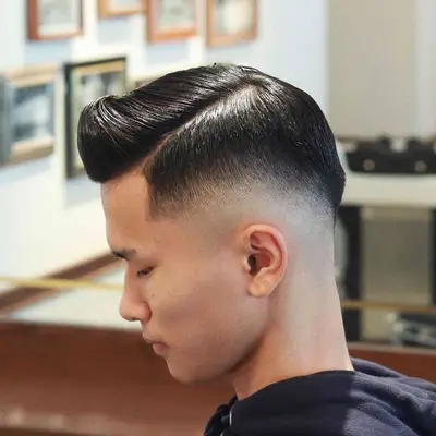 Side view of man with mid-skin fade haircut with side part and gel