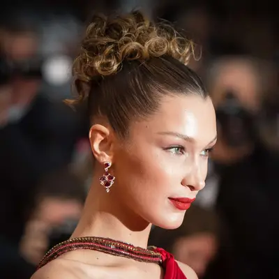 Bella Hadid wears a curly bun hairstyle with dark roots and light ends