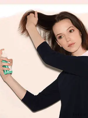 Close up of a model spraying sea salt spray into her short brown bob.