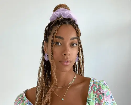 Woman wearing her braids half-up, half-down with a purple scrunchie