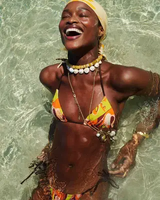 A woman in a colorful swimsuit in the water wearing a matching yellow bandana