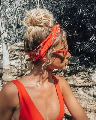 A blonde women with curly hair wearing a messy bun and red bandana