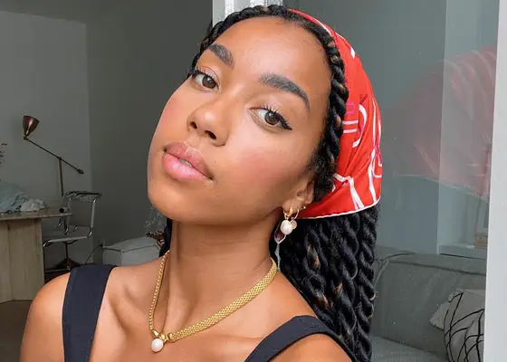 A person wearing a red bandana and gold jewelry, with braided hairstyle