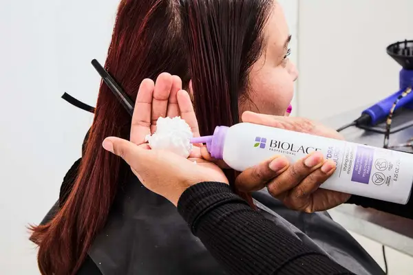 A person applies Biolage Hydra Source Styling Mousse to the palm of their hand