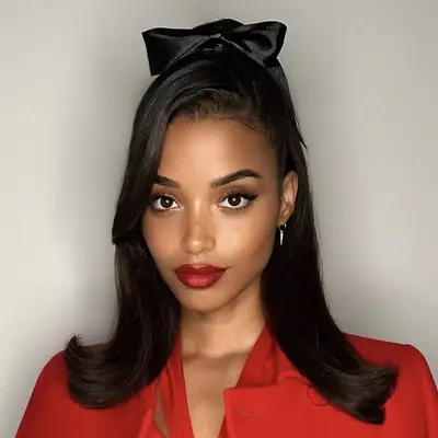 Person with styled half-up half-down hair and a bow, wearing a red outfit