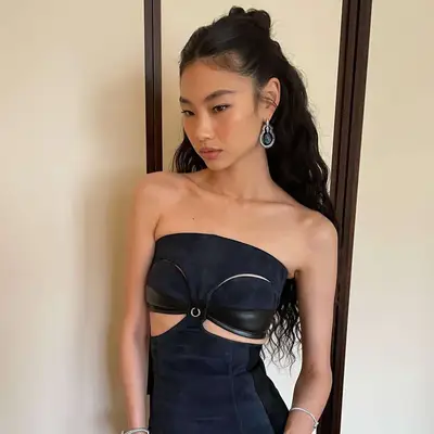 A person standing indoors wearing a strapless outfit with cut-out details and elegant jewelry