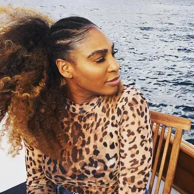 Serena Williams sitting near the water with a braided cornrow scalp and a voluminous curly ponytail