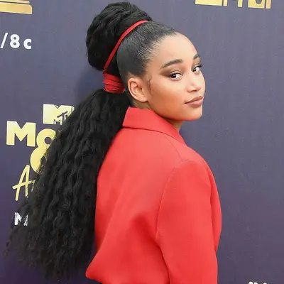 Amandla Stenberg wears a wavy high ponytail with red string creating two sections
