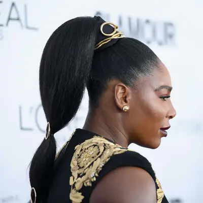 Serena Williams wears a sleek high bubble ponytail with gold accessories