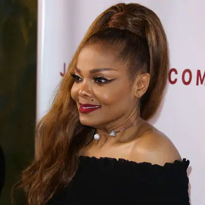 Janet Jackson wears a high ponytail with sleek roots, a wrapped base, and voluminous ends