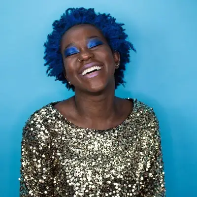 A laughing woman in a glittery dress has a head of vibrant blue hair