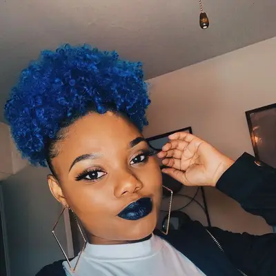 A model with a dark lip and geometrical earrings has midnight-blue curls 