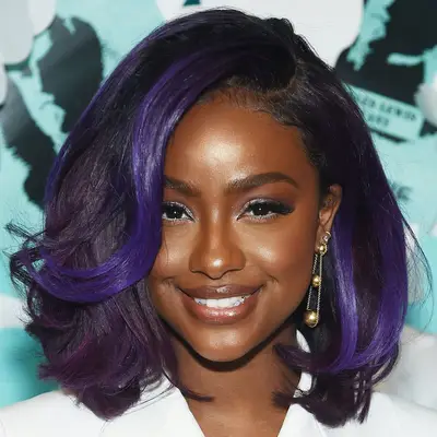 Justine Skye wears a voluminous bob hairstyle with purple highlights