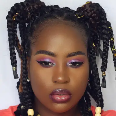 A woman with chunky box braids in two half-up pigtails with gold accessories