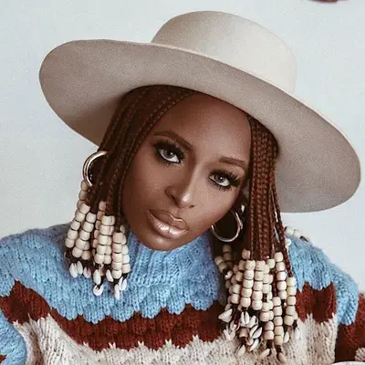 A woman with short, brown beaded box braids and a white hat