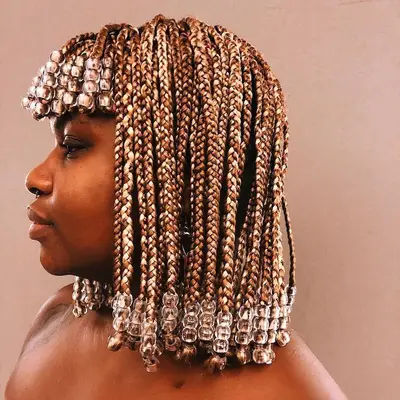 A woman with short mixed brown box braids and blunt bangs embellished with clear jumbo beads