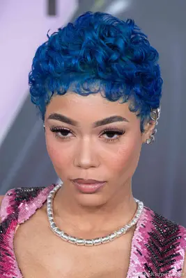 Justine Skye with long, bright purple hair, smoky eyeshadow, and neutral glossy lips