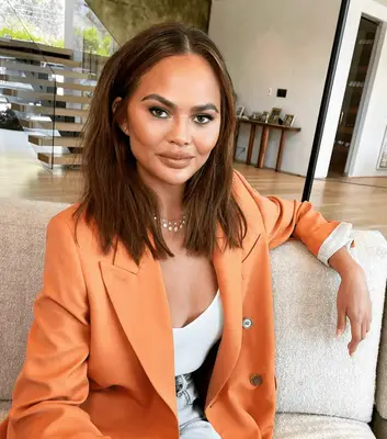 Chrissy Teigen in orange blazer with tousled lob
