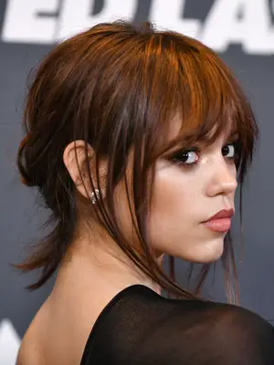 jenna ortega with bangs and side pieces hanging out with hair pulled back into loose low bun