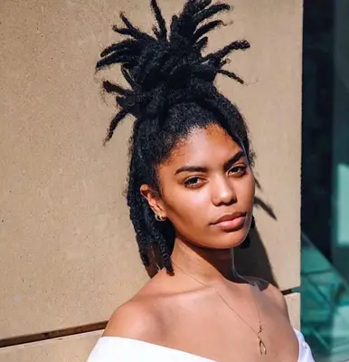 A person leaning against wall wearing freeform locs