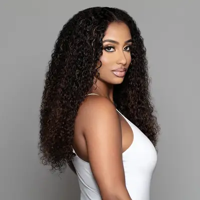 A person wearing curly hair extensions in front of a gray background