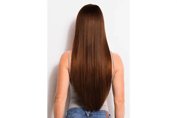 The back of a person wearing long brown hair extensions facing a white background