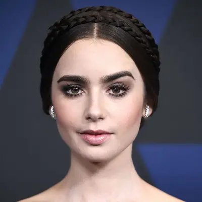 Lily Collins wears a sleek middle-part updo with crown braids