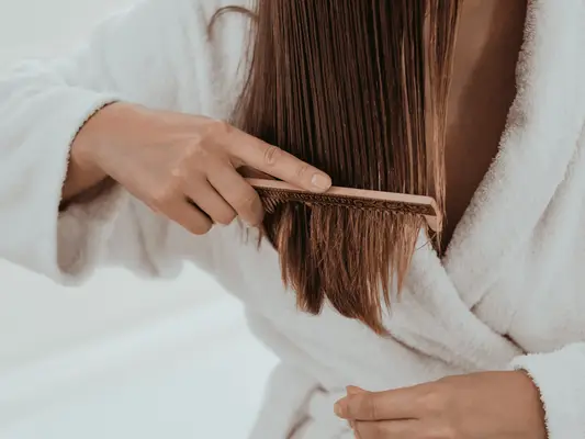 A woman in a robe using a wooden comb to brush through the ends of her hair