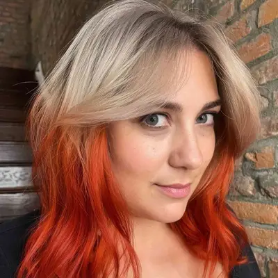 Woman with dark roots to ashy blonde to fiery red reverse ombré hair