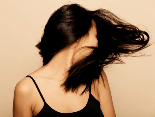 A woman with dark shiny hair splayed in front of her face as she turns her head