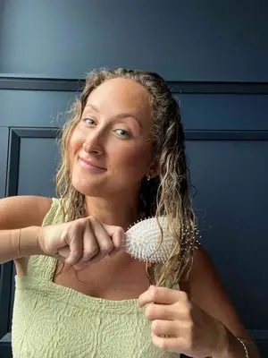 A person brushes their hair using the Dae Vegan Detangle + Style Brush