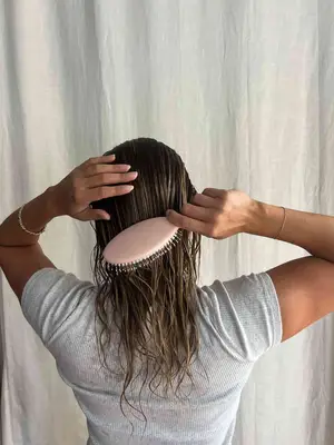 A person brushes their hair with the Dae Vegan Detangle + Style Brush