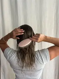A person brushes their hair with the Dae Vegan Detangle + Style Brush