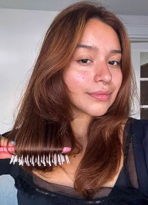 A person brushes their hair with the Fhi Heat UNbrush Detangling Hair Brush