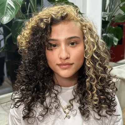 Model with brown curly hair and a blonde money piece.