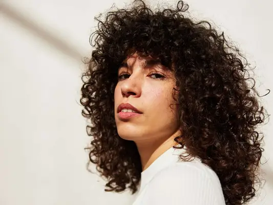 a woman with curly hair looks to the camera