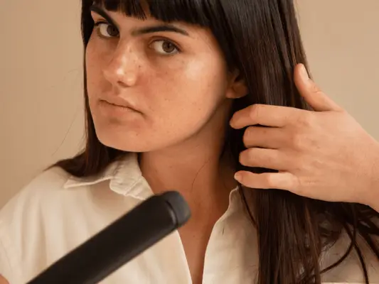 A woman holding her hair back in one hand and a flat iron in the other