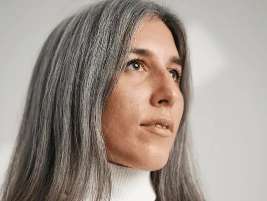 A woman in a white turtleneck growing out her gray hair