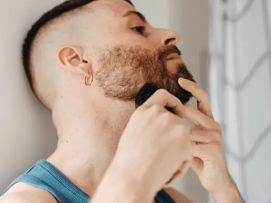 A man with a beard using an electric trimmer to shave