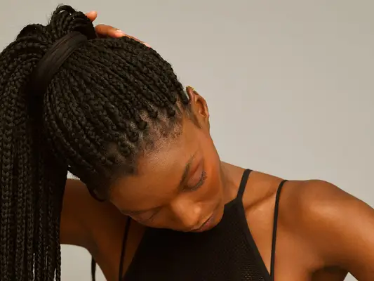 a woman with box braids in a ponytail, her gaze set down