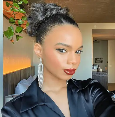 Olivia Hancock wearing silver dangly earrings, red lipstick, and curly undone bun