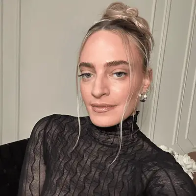 Hallie Gould with face framing pieces and romantic pinned back bun, black sheer long sleeve top