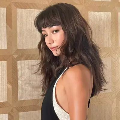 Natasha Liu Bordizzo posing from a side angle showing off thick, layered haircut with bangs