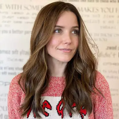 Sophia bush looking away from camera smiling with brown balayage, wavy hair at medium length