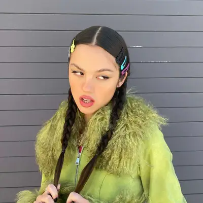 Olivia Rodrigo wearing colorful barrettes with two pigtail braids and a green furry jacket