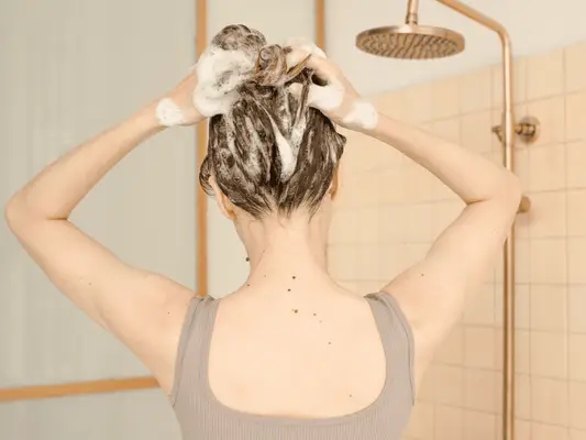 A woman in the shower with suds in her hair as she washes it