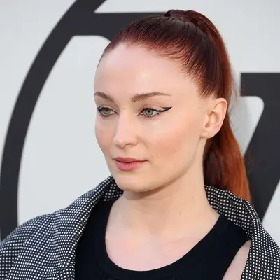 Sophie Turner wears a simple red high ponytail and graphic winged eyeliner