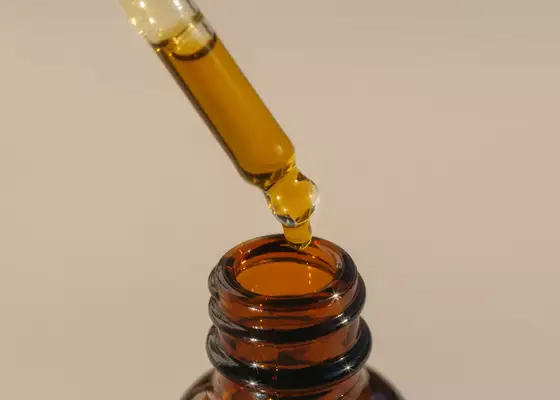 close up of golden oil dropper on tan background